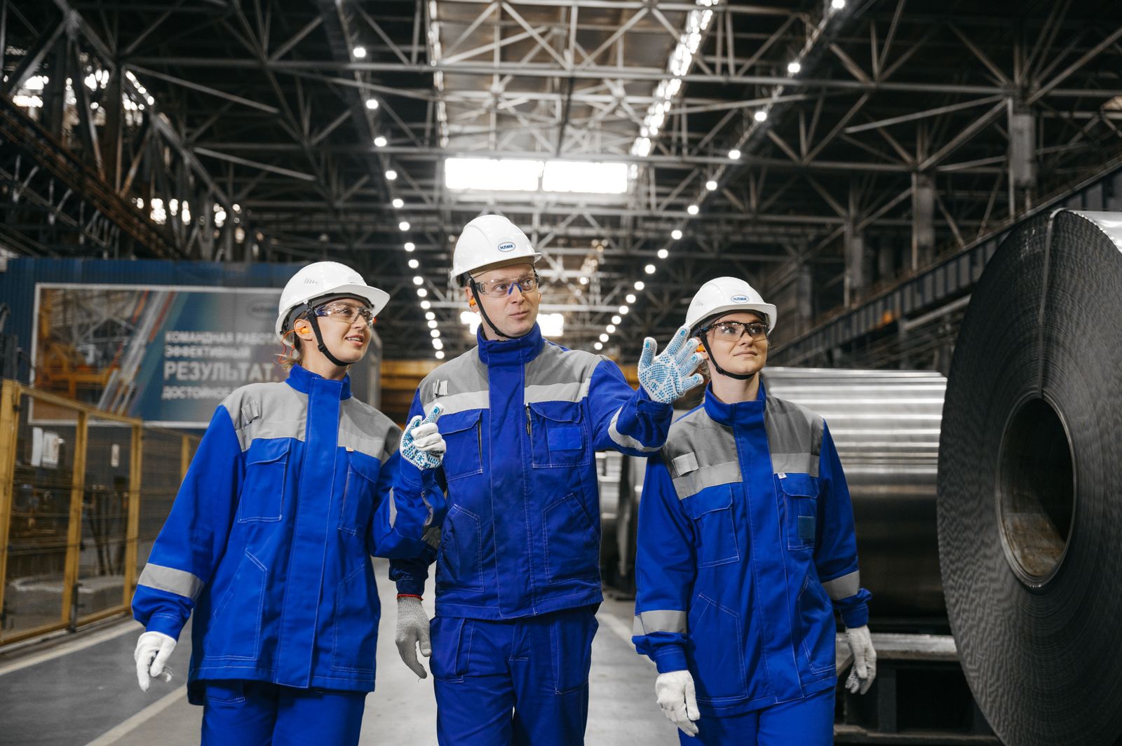 Three engineers in blue overalls and hard hats walking through a plant hall