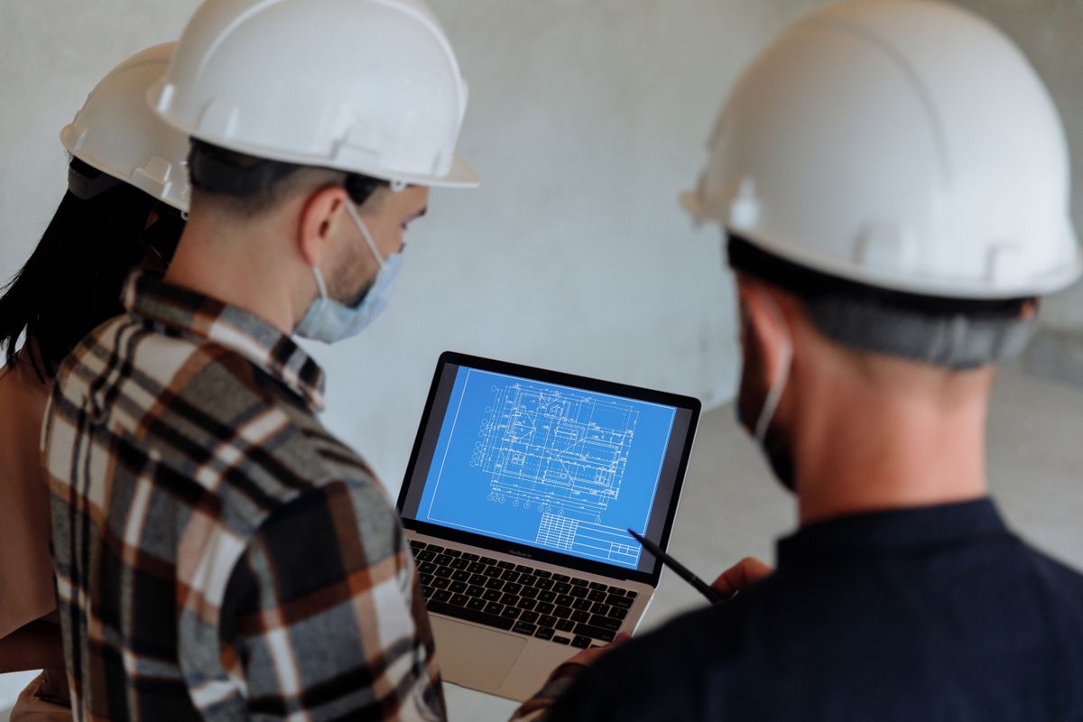 Engineers in hard hats reviewing a plant drawing on a laptop